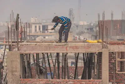 A worker on the top floor of a house under construction, column steel standing up, city rooftops behind