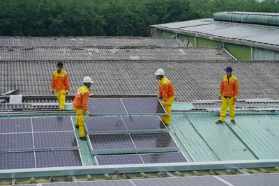 Installers in orange overalls laying solar panels on a roof