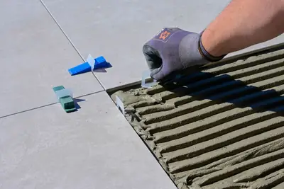 A gloved hand fitting tile levelling clips between new floor tiles